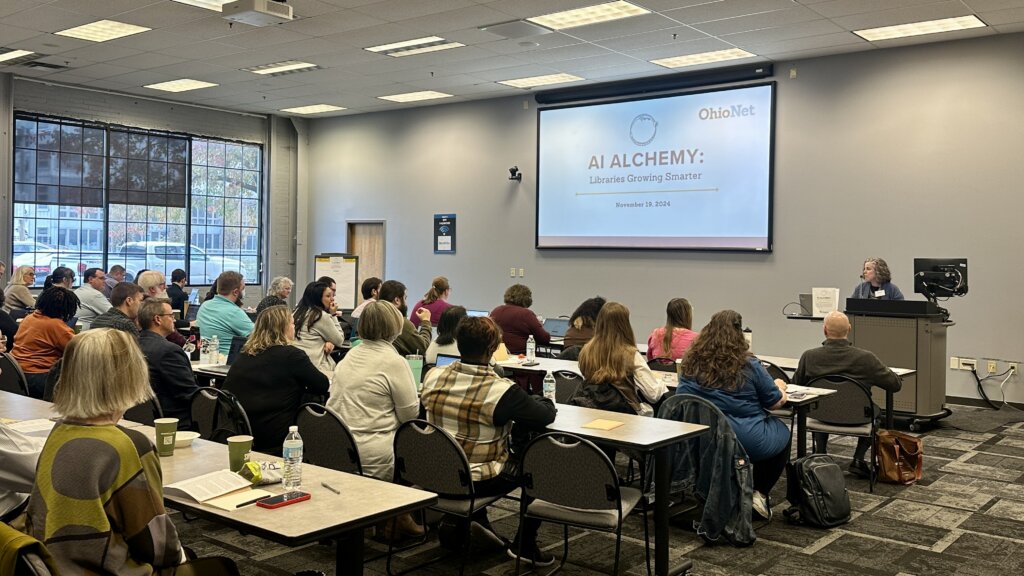 Attendees at OhioNet’s AI Alchemy: Libraries Growing Smarter event are greeted by OhioNet's Executive Director and CEO. A large screen at the front of the room displays the event title and date.